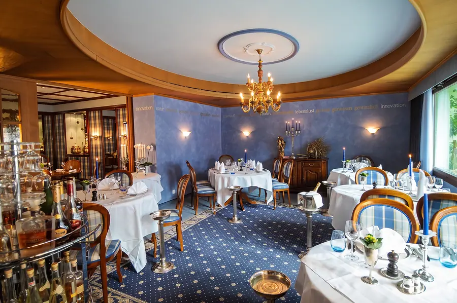 Saal mit blauen Wänden, Leuchter und weiss gedeckten Tischen